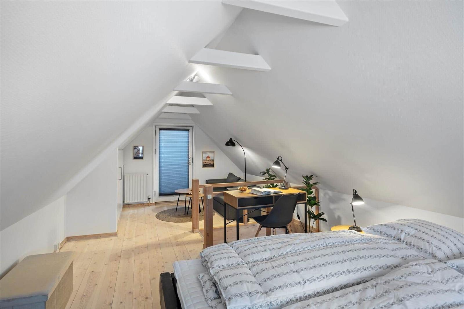 Schlafzimmer mit Doppelbett, Schreibtisch und Schlafbereich unter Dachschräge.