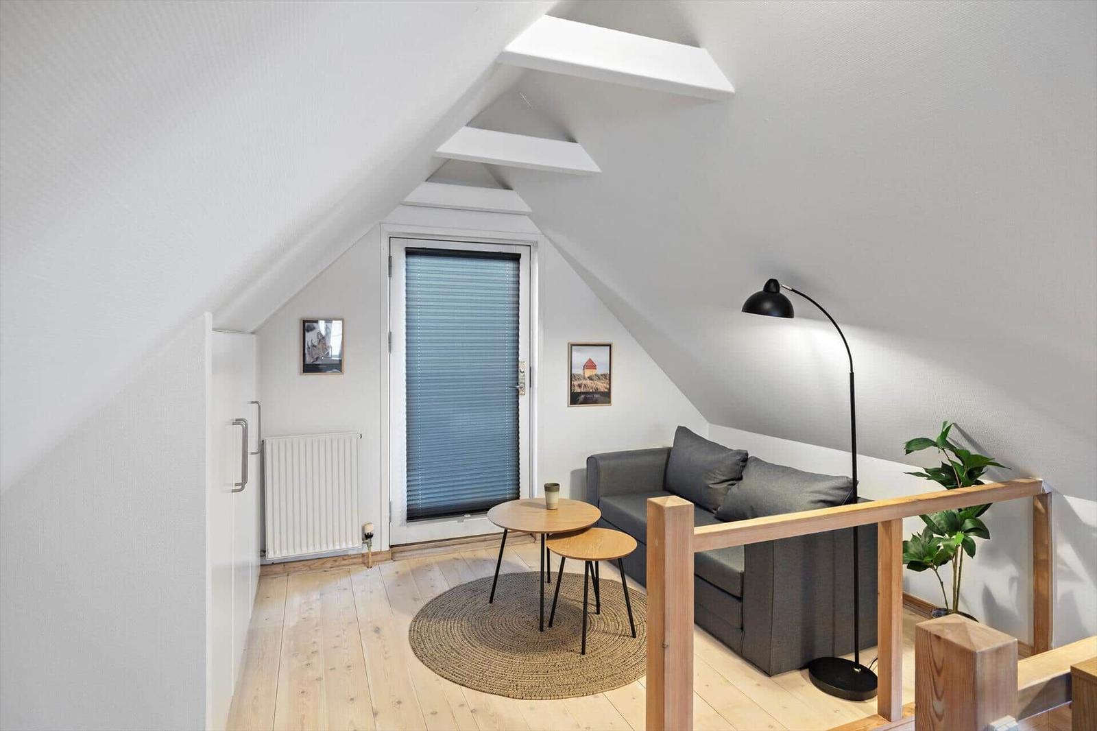 Dachgeschosswohnung mit Sofa, Tisch, Lampe und Pflanze.