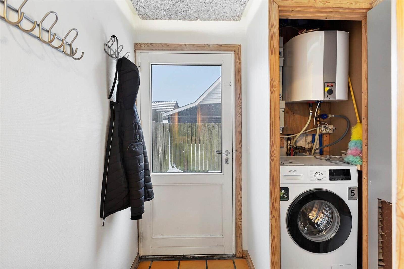 Eingangsbereich mit Waschmaschine und Heizungsraum. Jacke hängt an Haken.