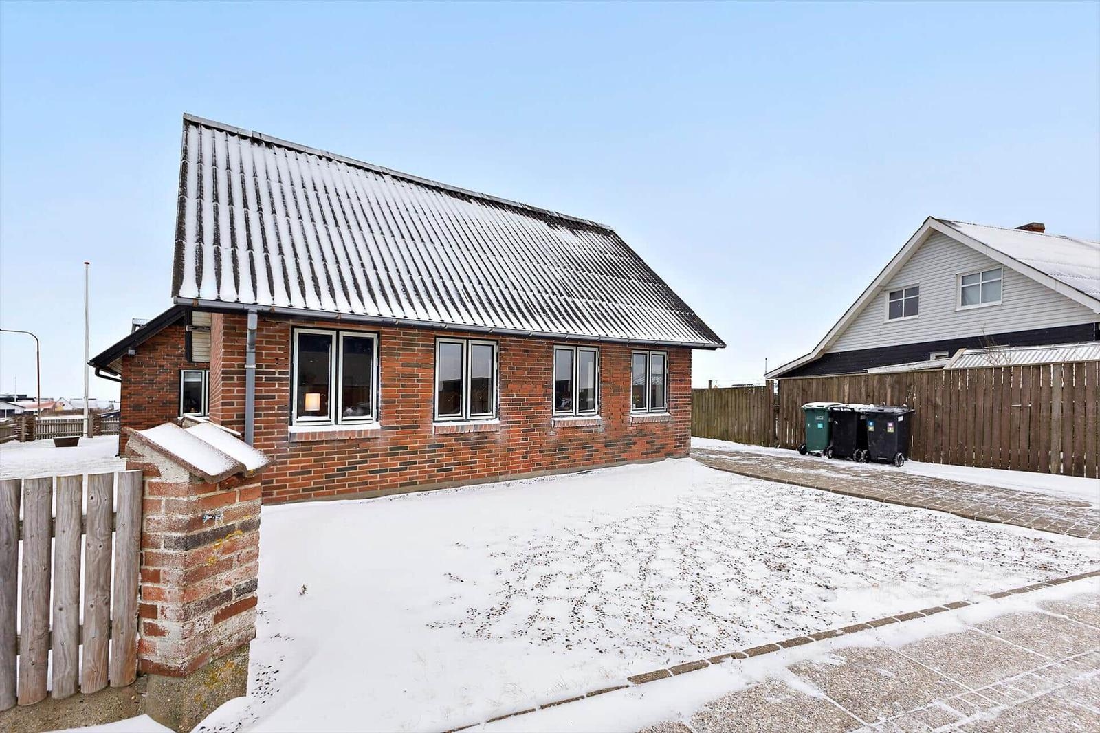 Rotes Backsteinhaus mit schneebedecktem Dach und Fenstern im Winter.