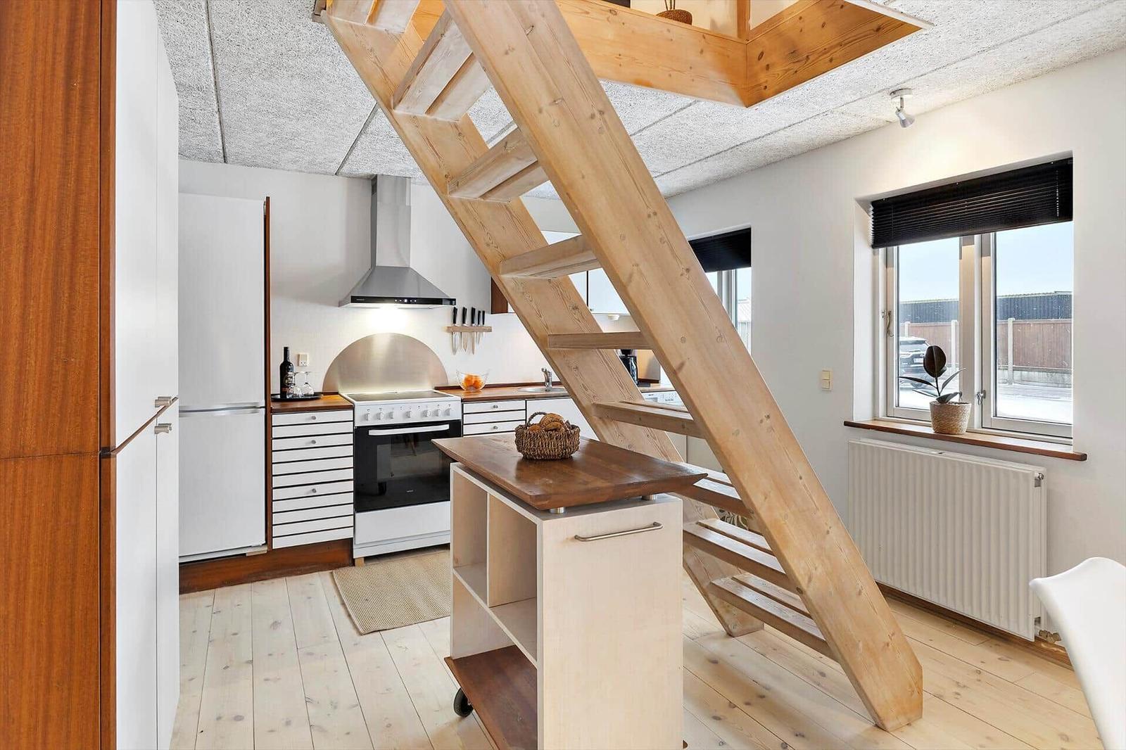 Küche mit Holztreppe zur oberen Etage. Fenster mit Pflanze und Heizkörper.