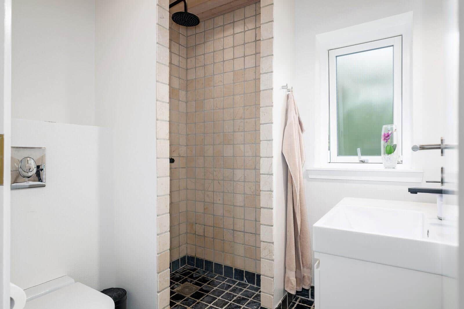 Bathroom with shower, sink, and toilet. Window with flower vase.