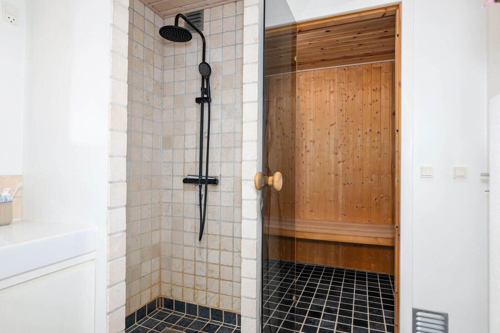 Shower with showerhead and sauna with wooden wall and bench.