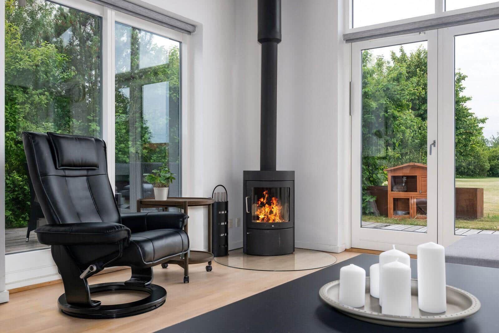 Black chair next to fireplace and windows with view of garden.