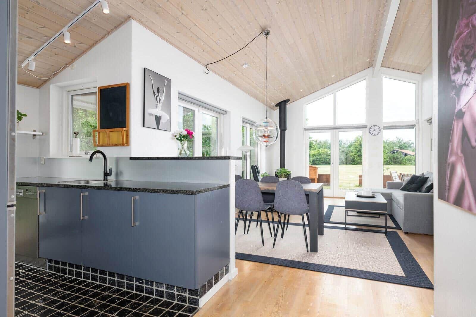Kitchen with dining area and living room with wooden ceiling and large windows.