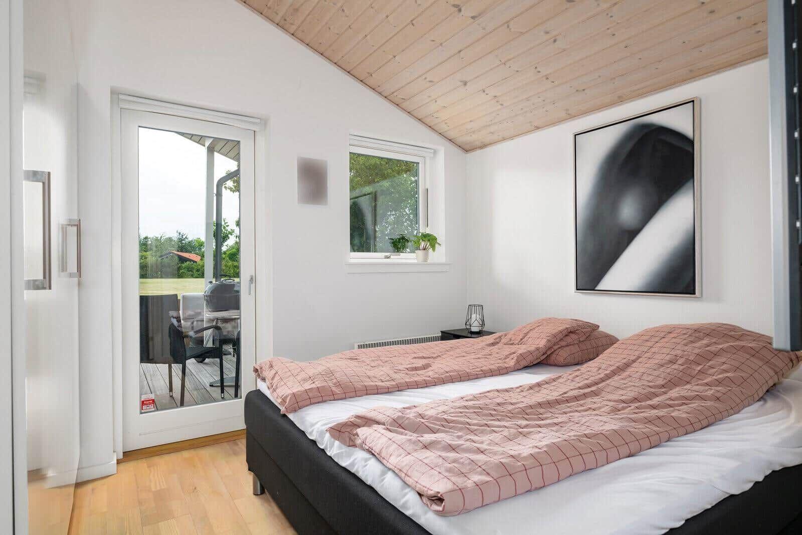 Bedroom with bed, door to balcony, and window. Wooden ceiling and wall art.