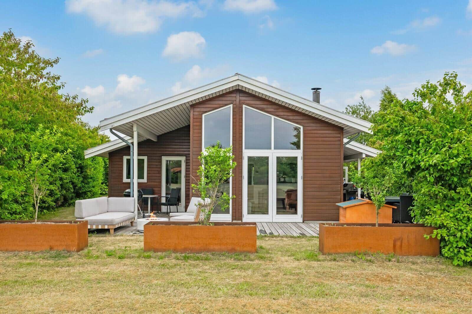 Modern wooden cabin with large windows and terrace with garden furniture.