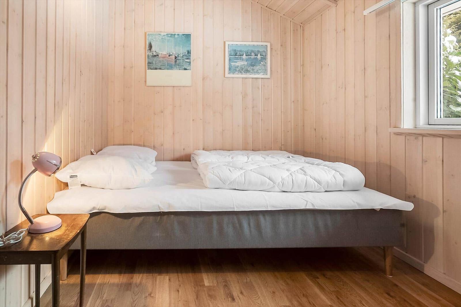 Bedroom with bed, nightstand, and window. Wooden walls and floor.