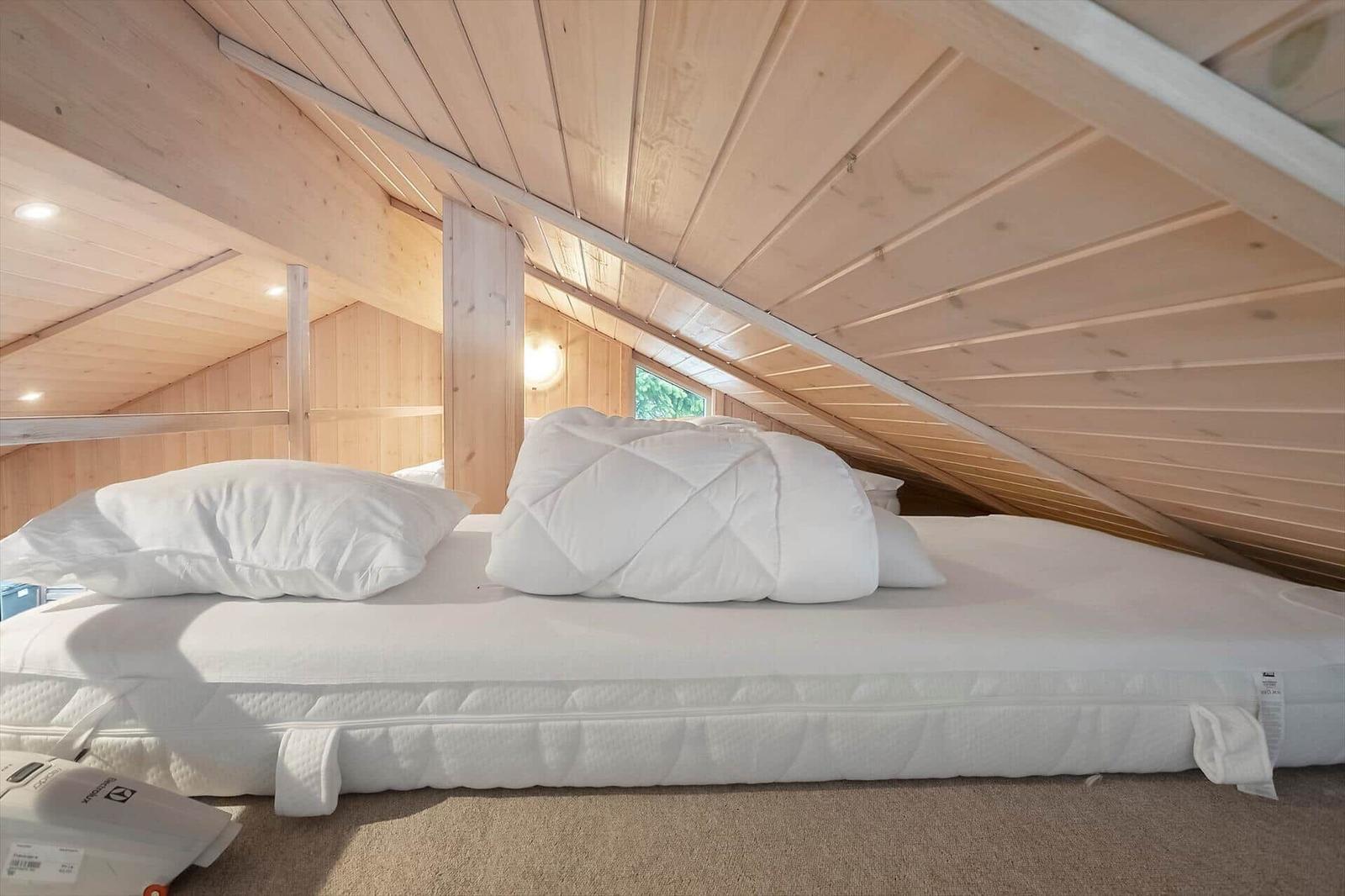 Double bed under sloped roof with wooden walls and window