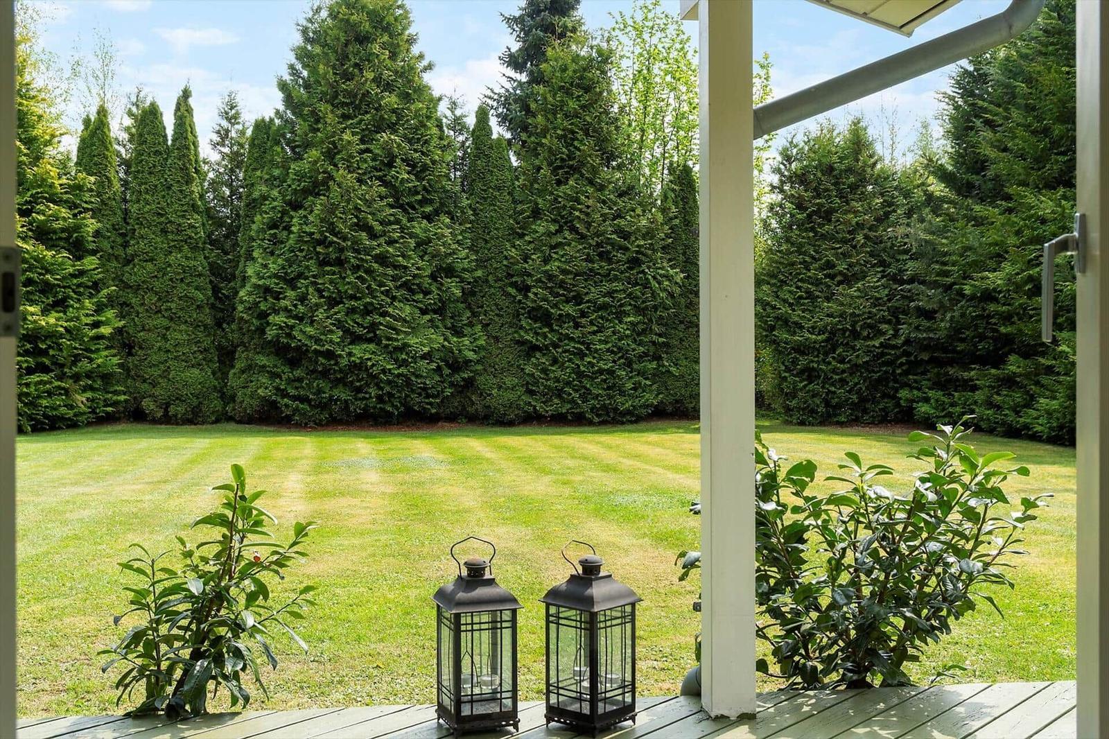 From the porch, you see a green lawn and tall evergreen trees.
