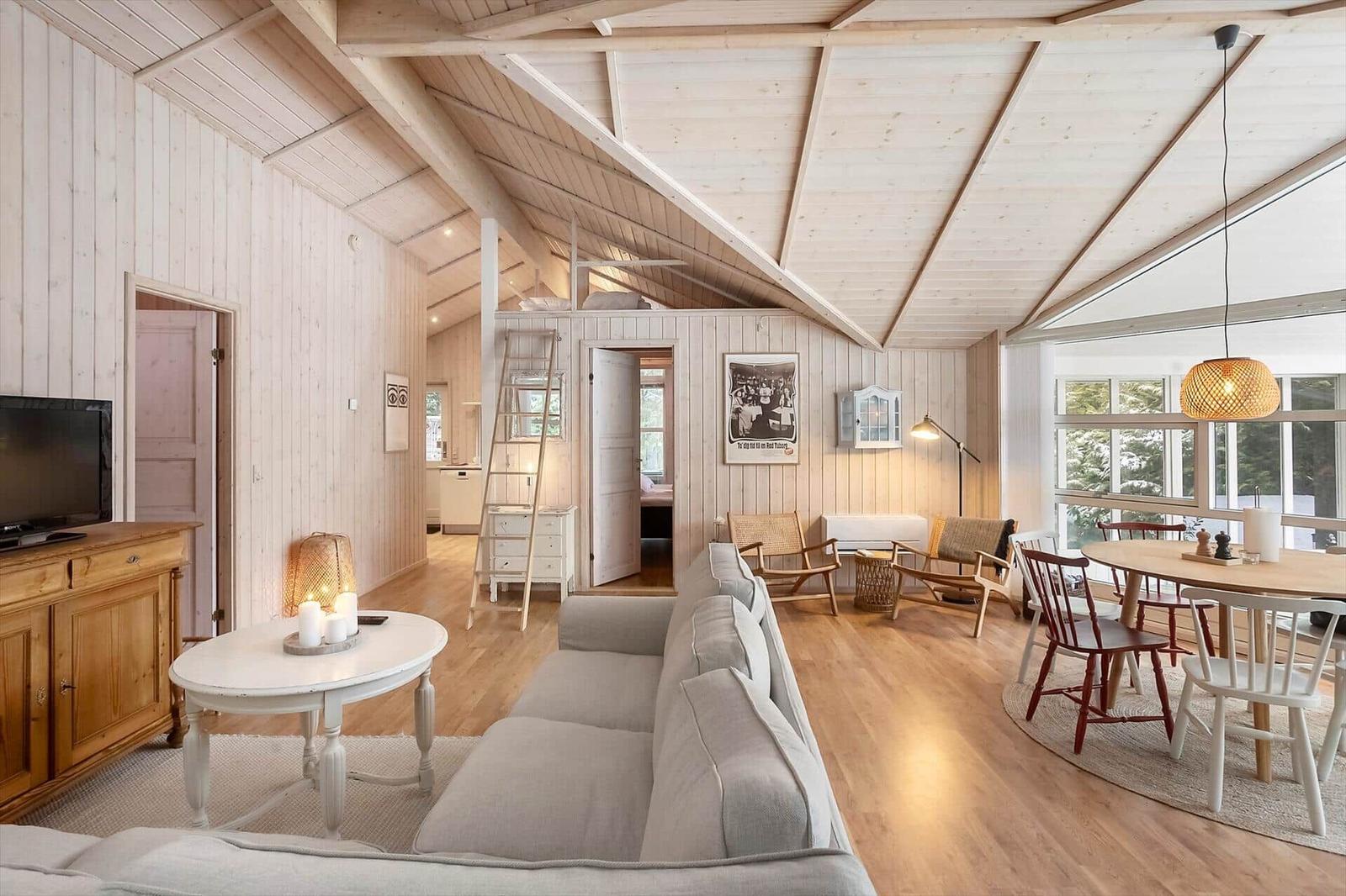 Living and dining area with wooden ceiling, sofa, table and chairs. Access to kitchen and bedroom.