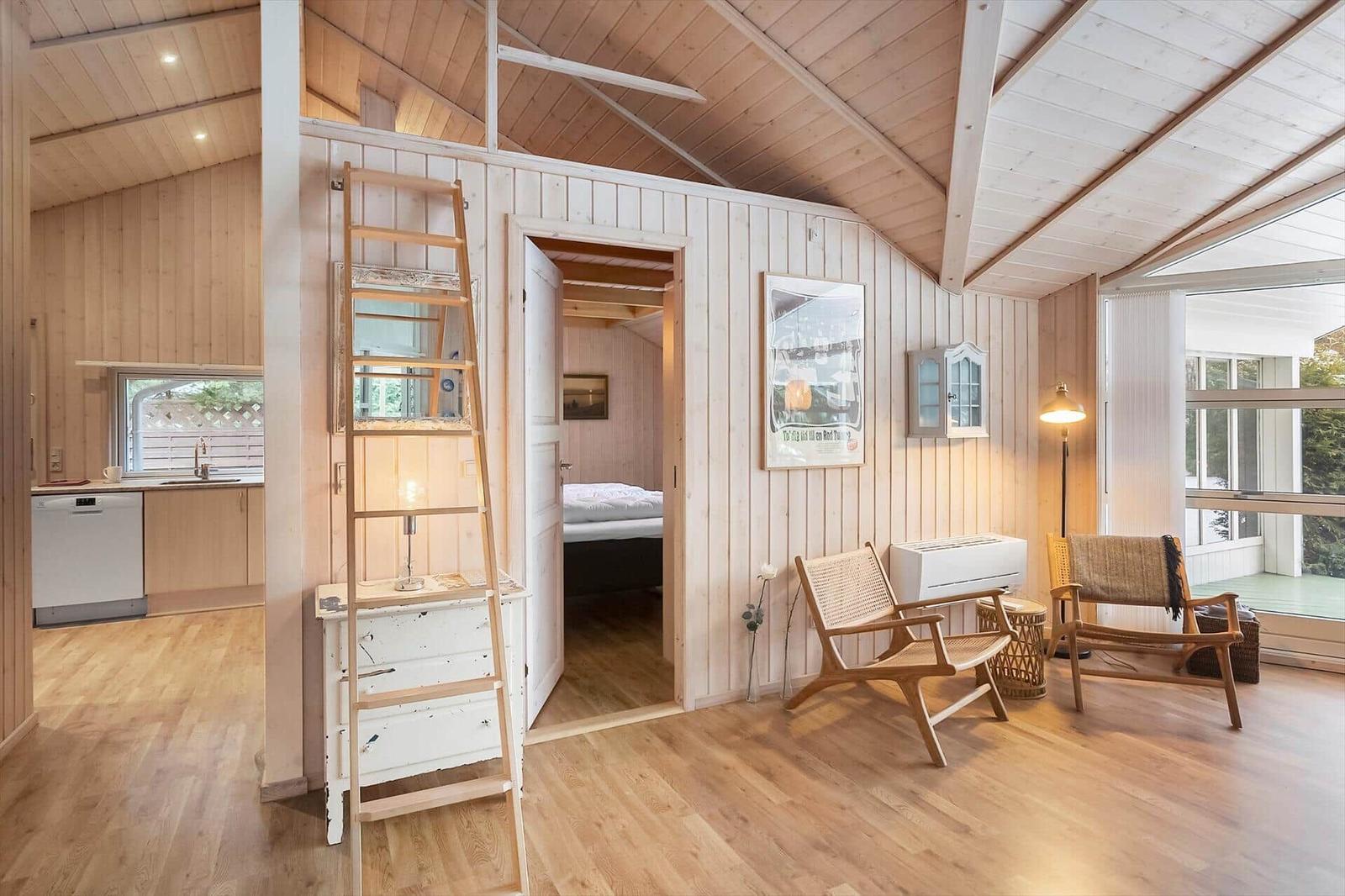 Living area with fireplace, bedroom, and kitchen. Wooden ceiling and walls.
