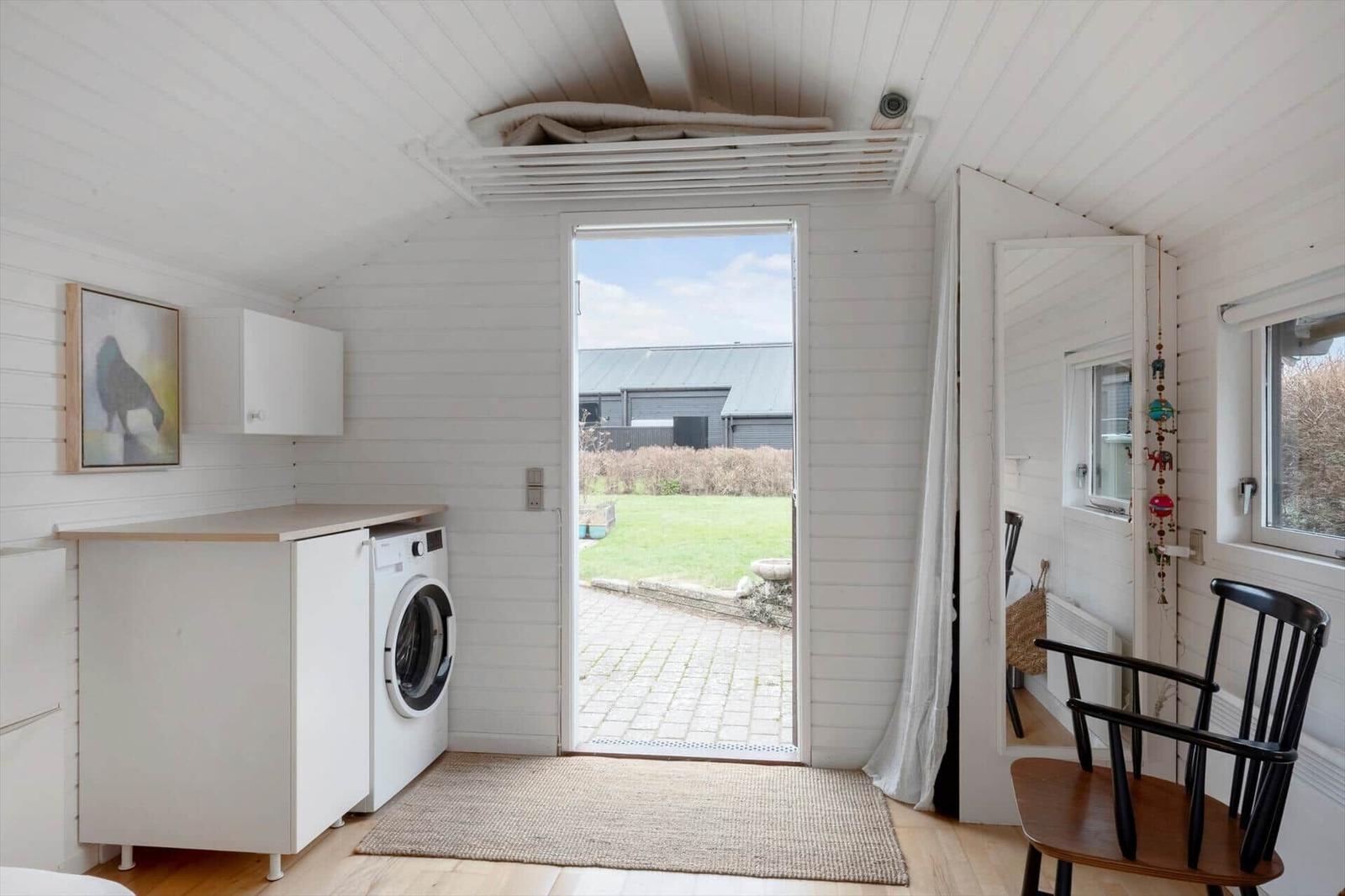 Wohnraum mit Waschmaschine, Tür zum Garten und Stuhl.
