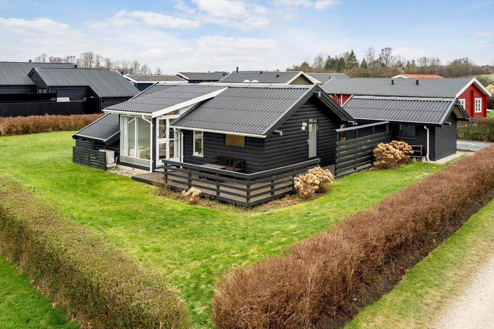 Schwarzes Holzhaus mit Terrasse und grünem Garten. Modernes Design mit Glasfront.