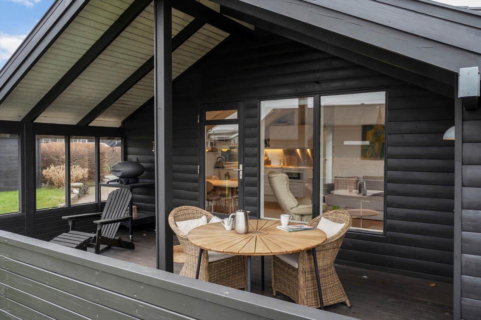 Terrasse mit Tisch, Stühlen und Grill. Blick ins Innere mit Küche und Wohnbereich.