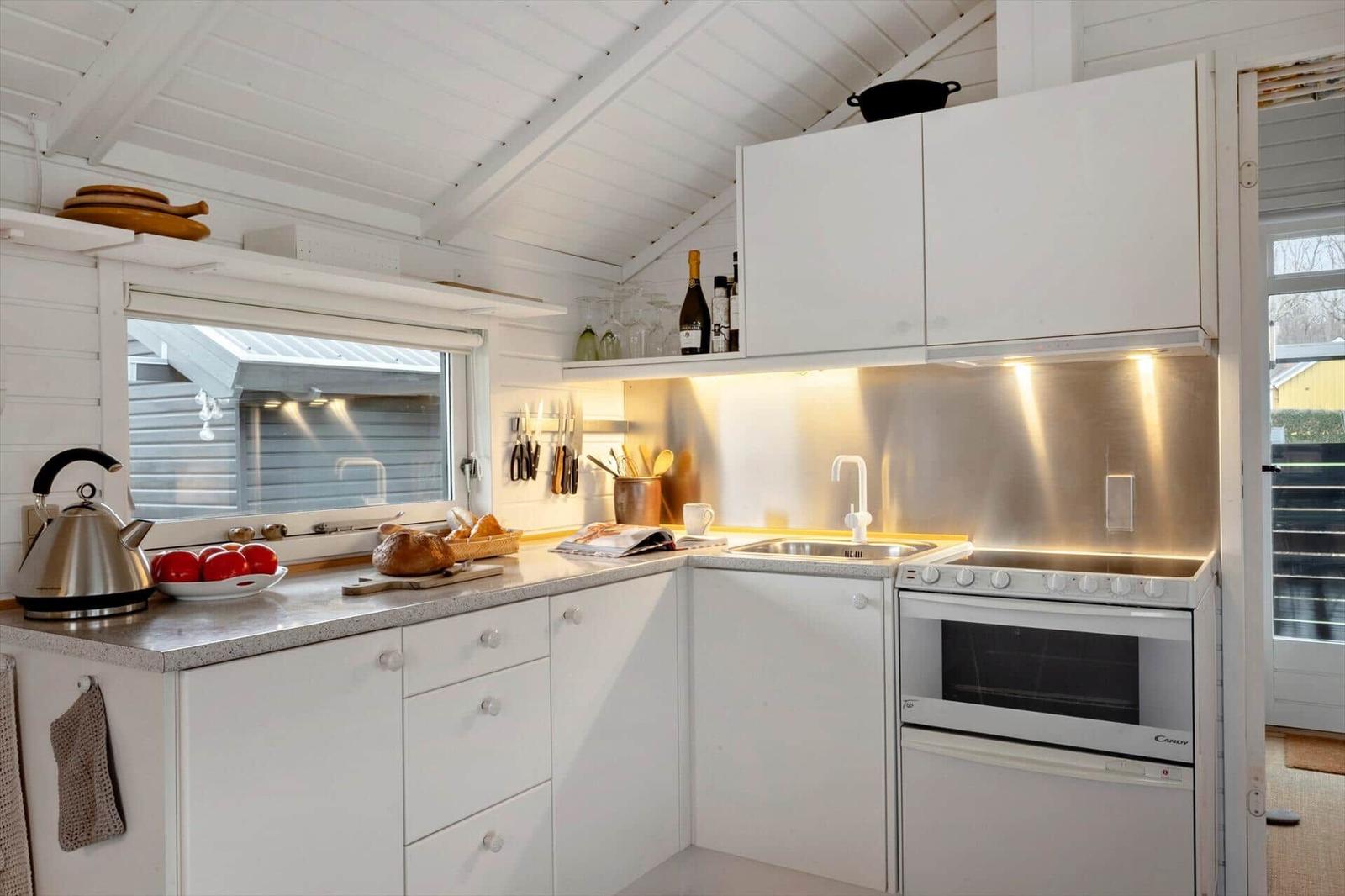 Küche mit weißen Schränken, Edelstahlspüle und Kochfeld. Fenster und Arbeitsfläche sichtbar.