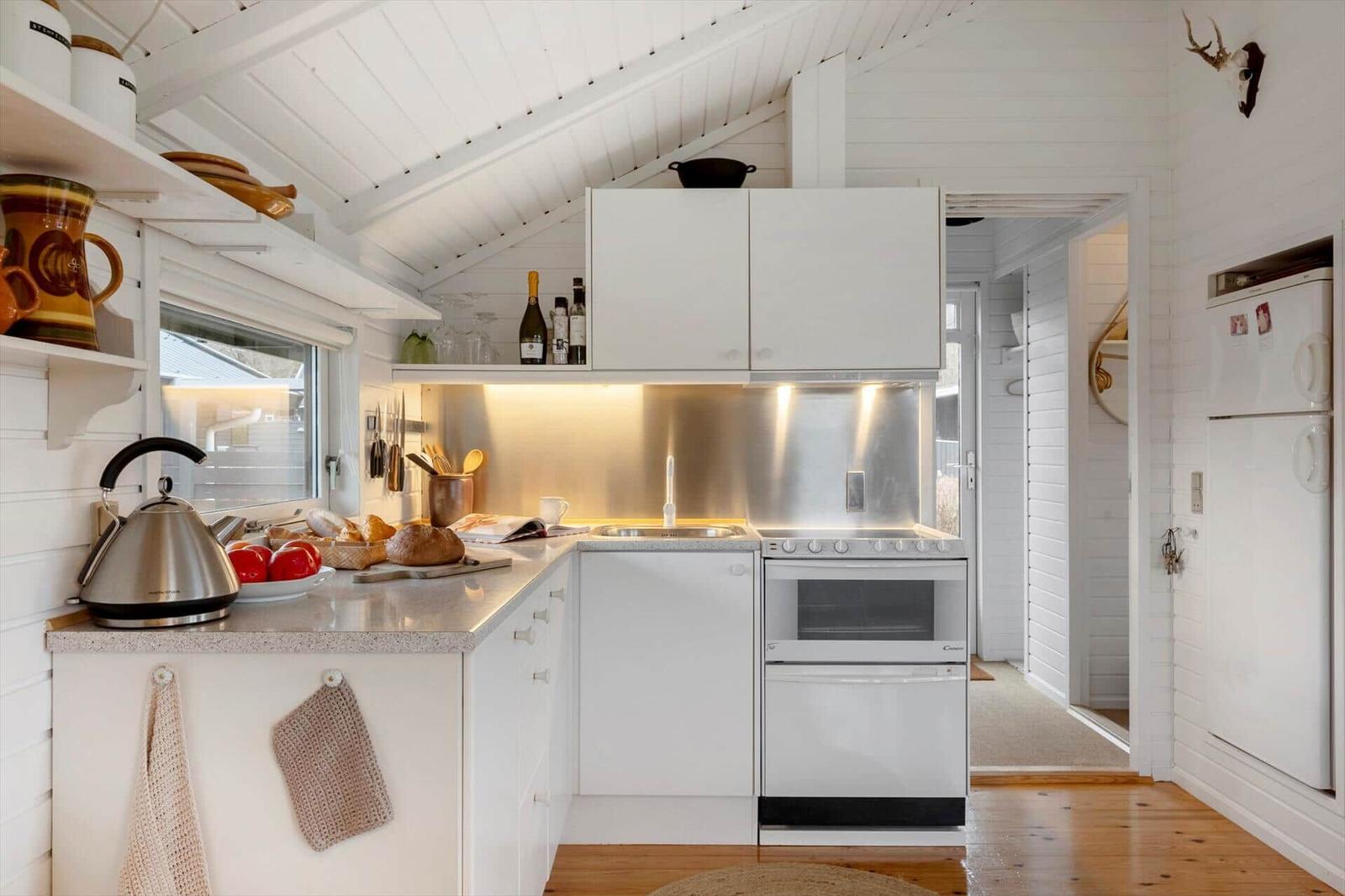 Küche mit weißen Schränken, Edelstahlspüle und Kühlschrank an der Wand.
