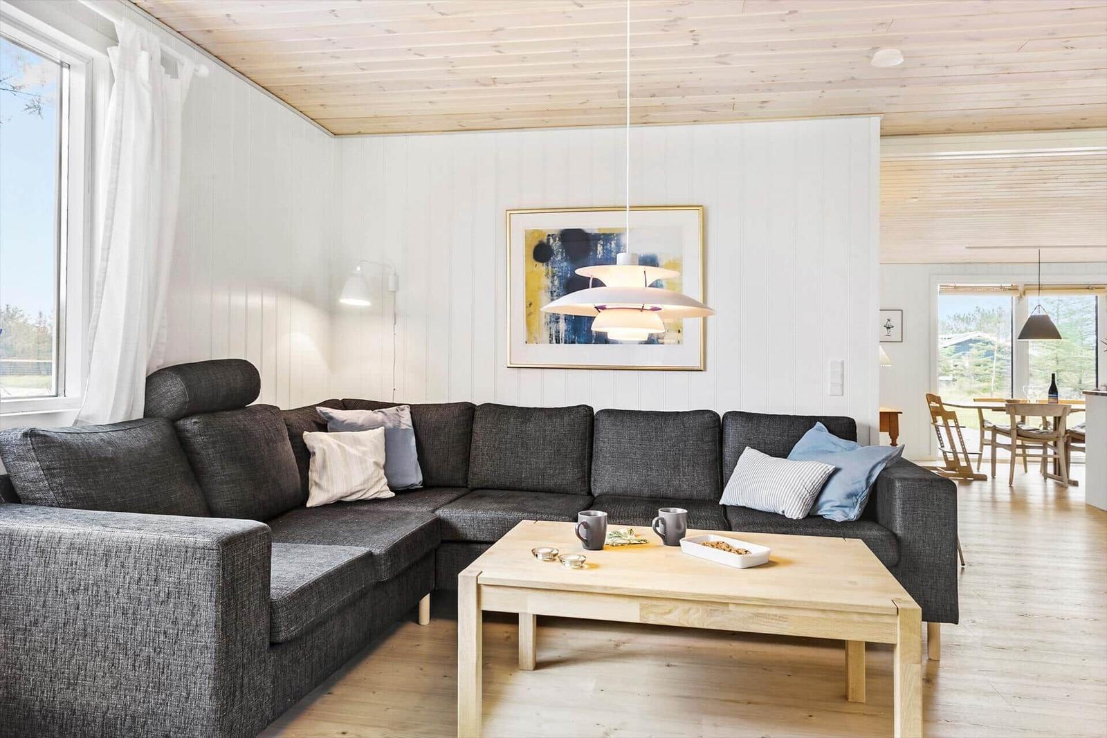 Ein Wohnzimmer mit grauem Sofa, Holztisch und weißen Wänden.