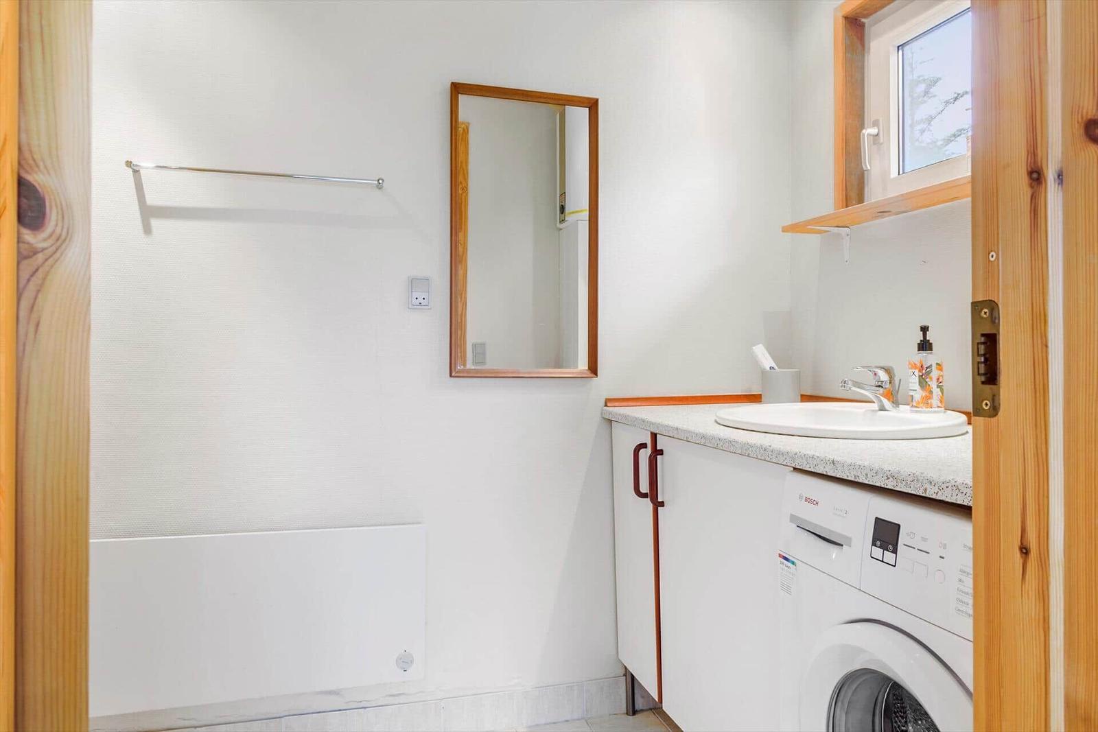 Badezimmer mit Waschmaschine, Spüle und Spiegel an der Wand.