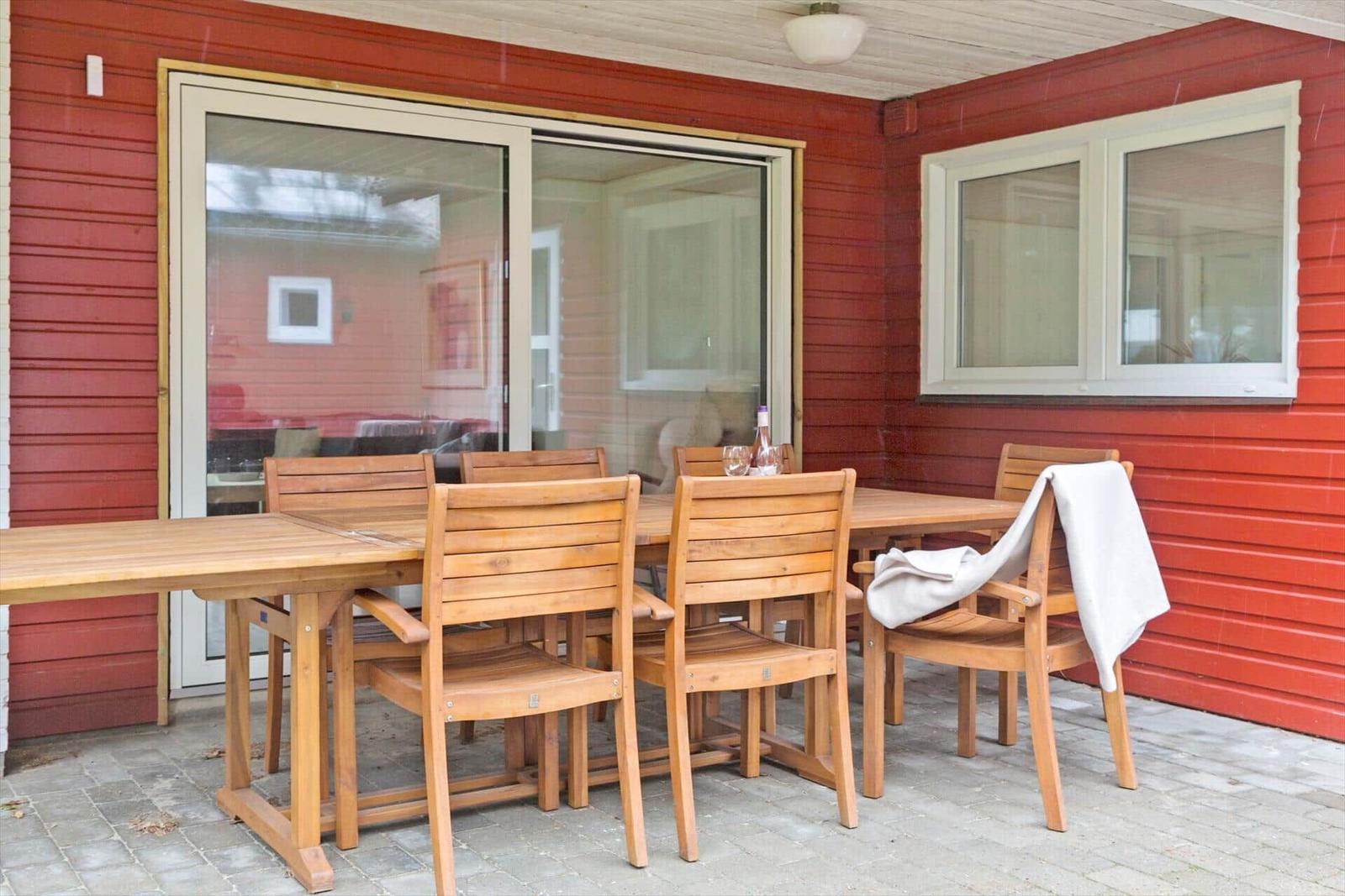 Terrasse mit Holztisch und Stühlen, rote Fassade, Fenster und Glastür.