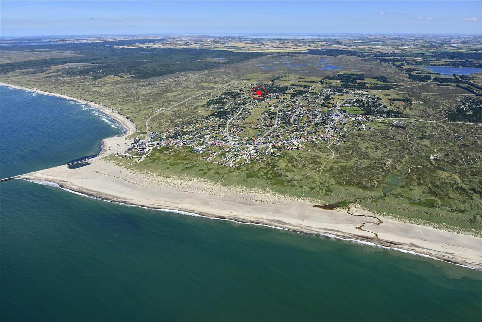 Luftbild eines Küstenorts mit Strand und grünen Hügeln. Ein roter Punkt markiert die Lage.