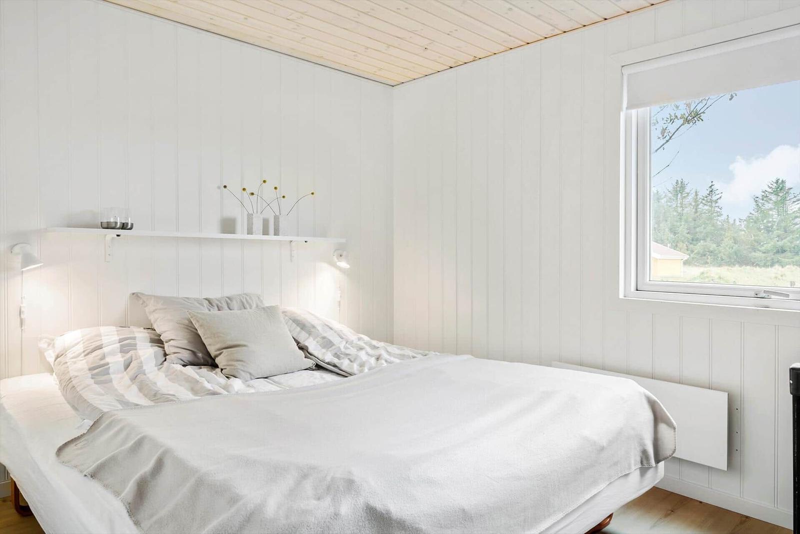 Schlafzimmer mit Bett, Fenster und weißen Wänden.
