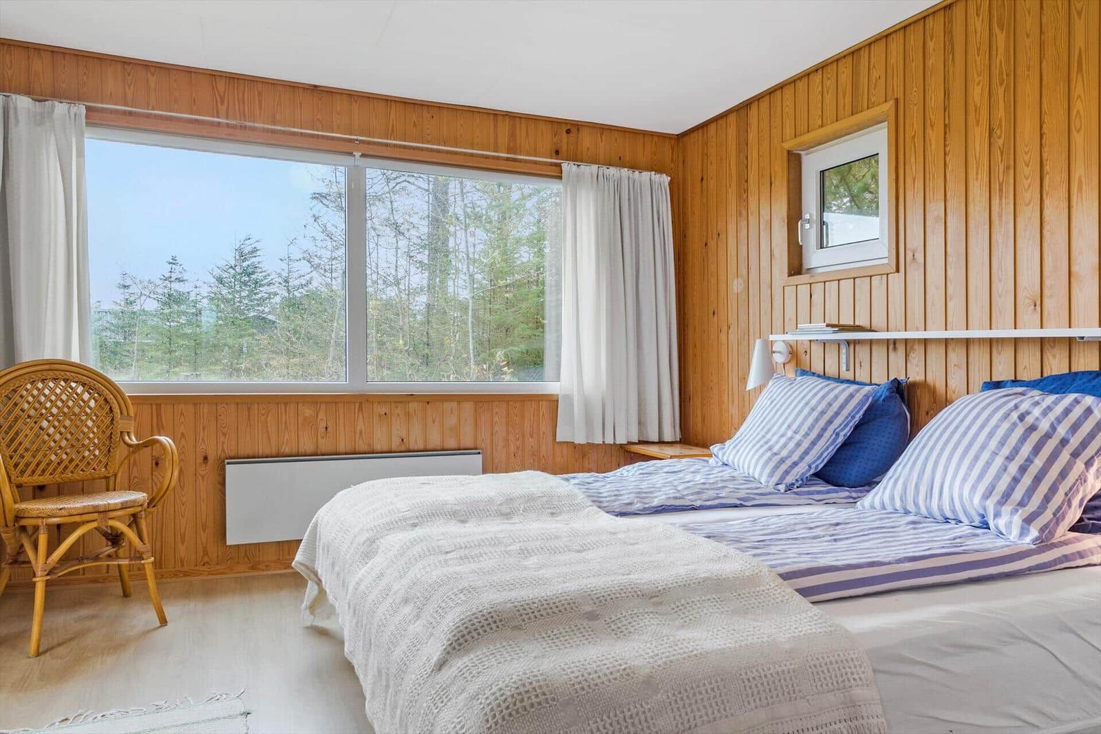 Schlafzimmer mit Holzwand, großem Fenster und Stuhl.