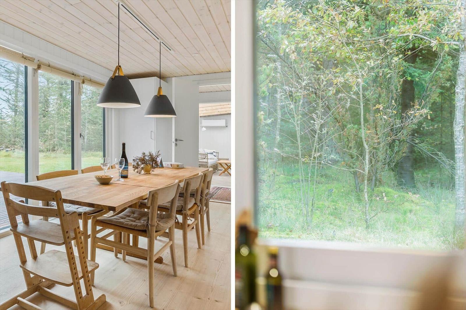 Esszimmer mit Holztisch und Stühlen, großes Fenster mit Blick auf Wald.
