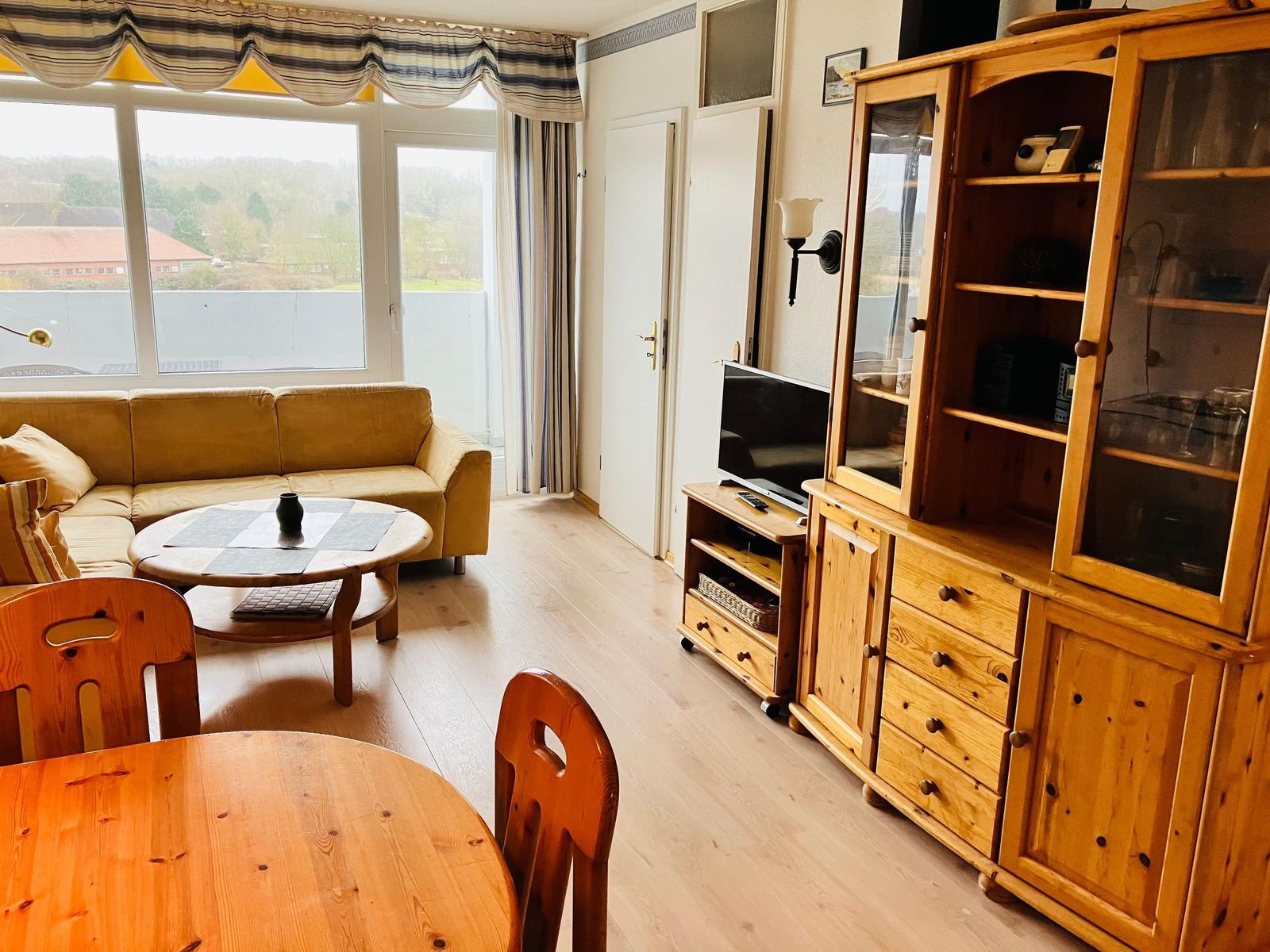 Wohnzimmer mit Sofa, Esstisch und Holzschrank. Große Fenster mit Blick.