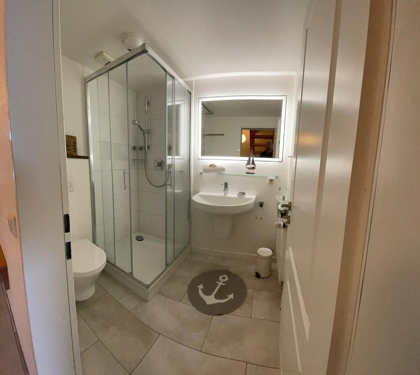 Badezimmer mit Dusche, Waschbecken und Toilette. Bodenmatte mit Ankermotiv.