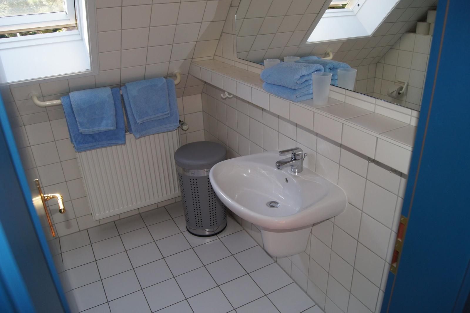 Badezimmer mit Waschbecken, Spiegel, Handtüchern und Fenster.