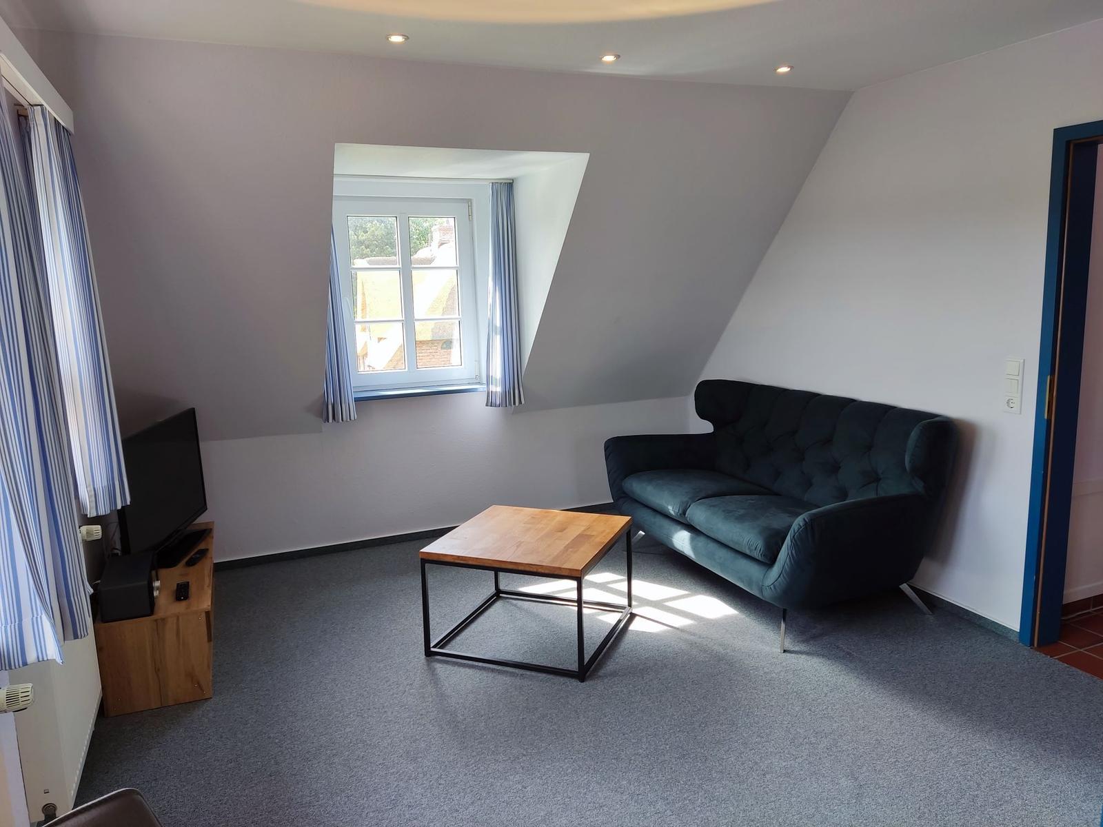 Wohnzimmer mit Sofa, Tisch und Fenster. Wandfarbe hell, Boden belegt.