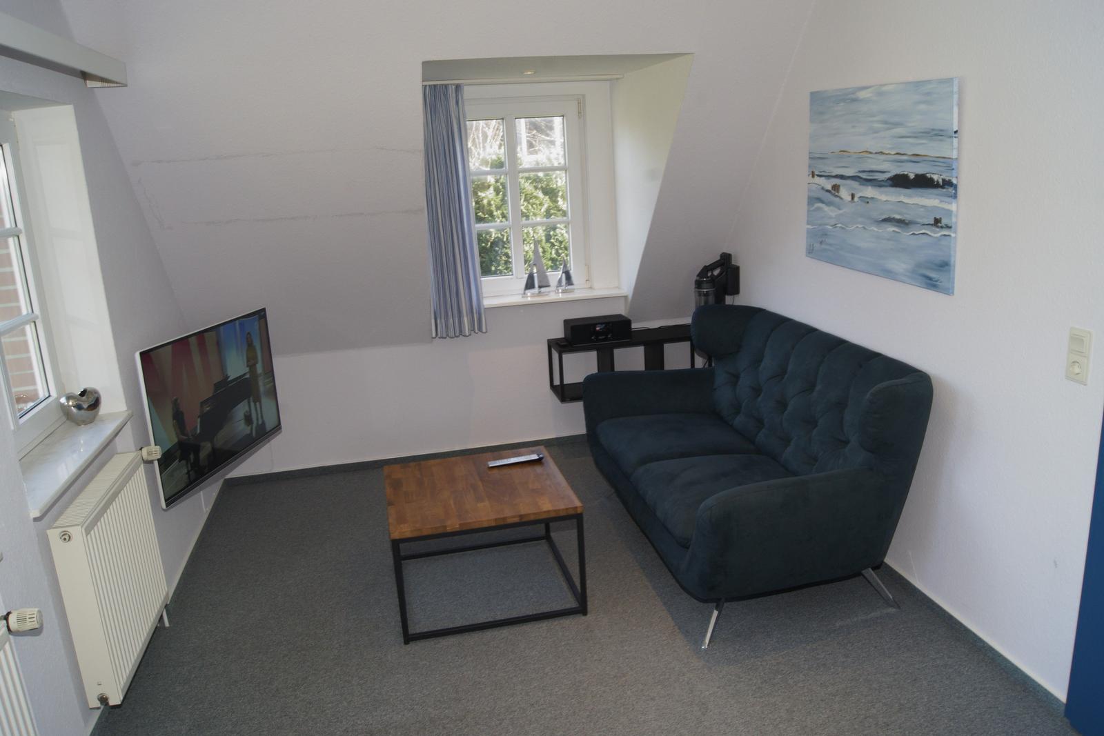 Ein Wohnzimmer mit Sofa, Couchtisch und Fernseher an der Wand.