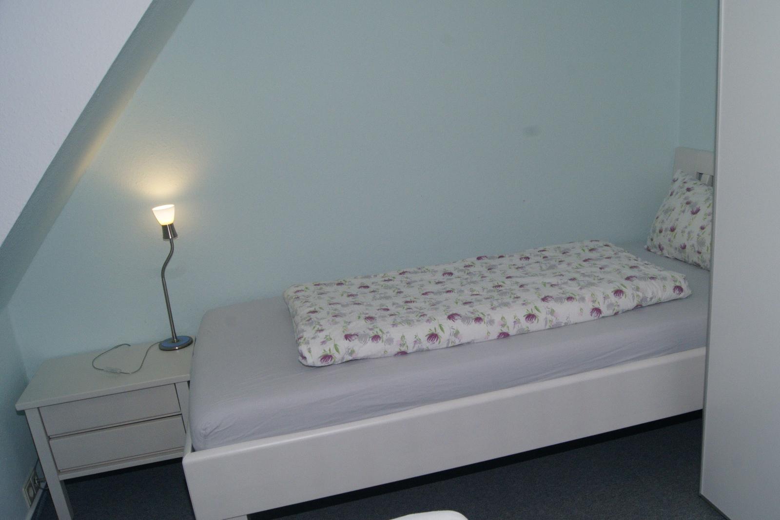 Schlafzimmer mit Bett, Nachttisch und Lampe unter Dachschrägen.