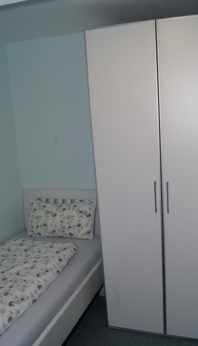 Schlafzimmer mit Einzelbett und weißem Schrank