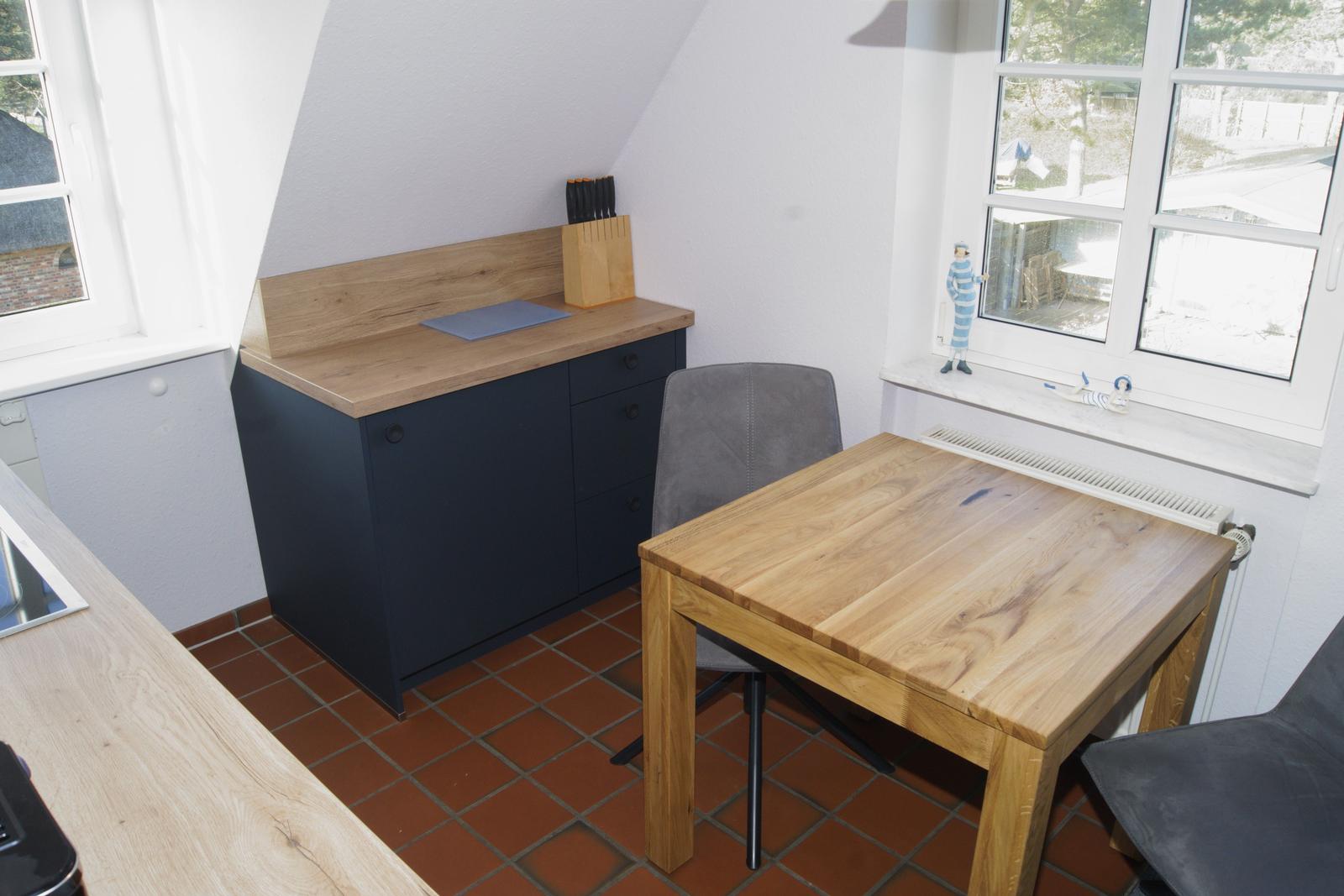 Küche mit Holztisch, Stühlen und dunklem Schrank. Fenster mit Blick nach draußen.