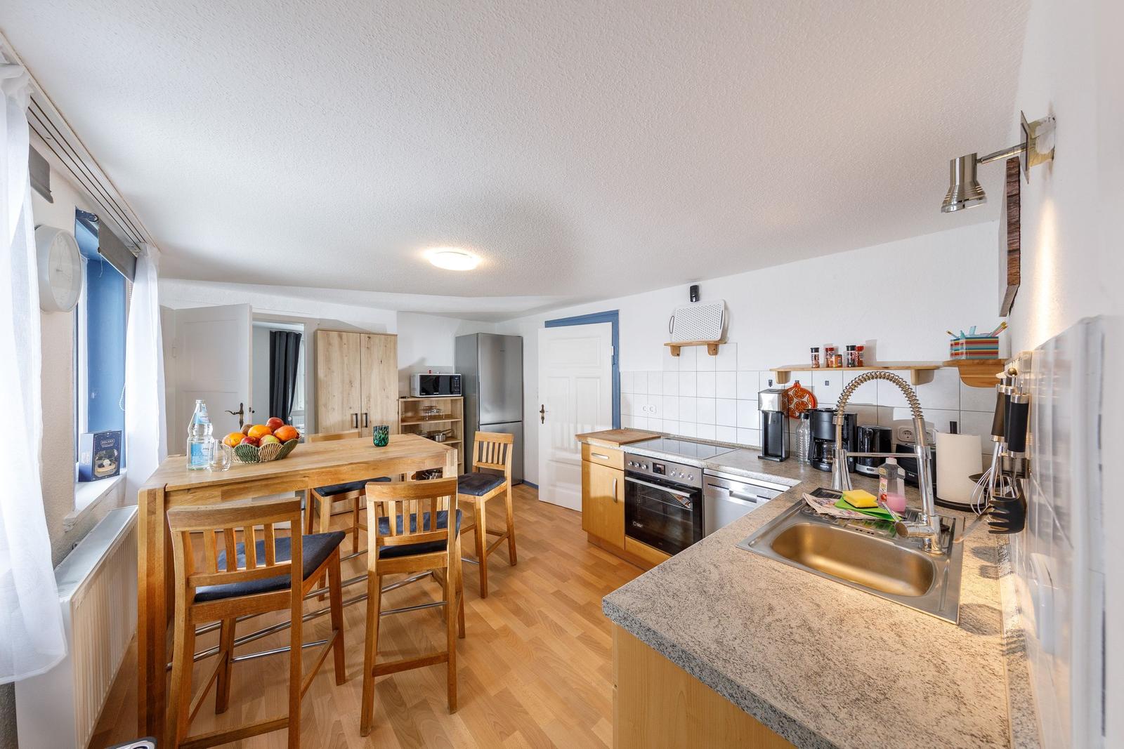 Küche mit Essbereich, Holztisch, Stühle, Spüle und Kochgeräte.