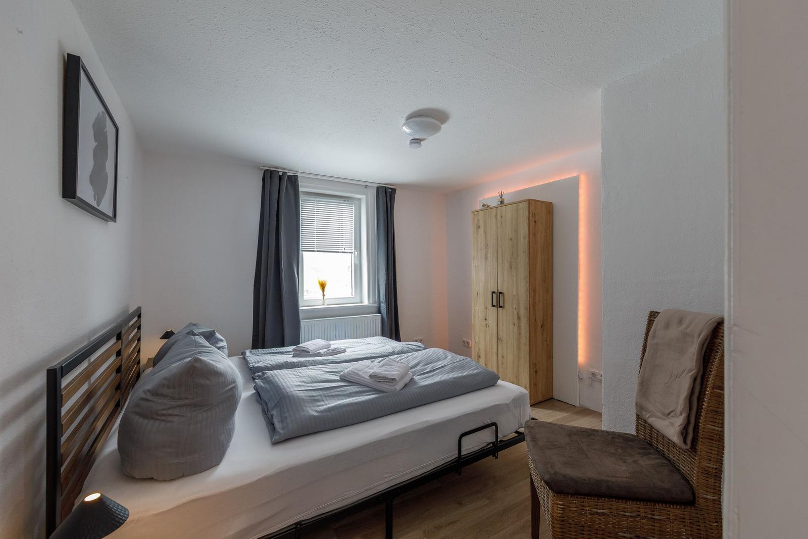 Schlafzimmer mit Doppelbett, Holzschrank und Fenster mit Vorhängen.