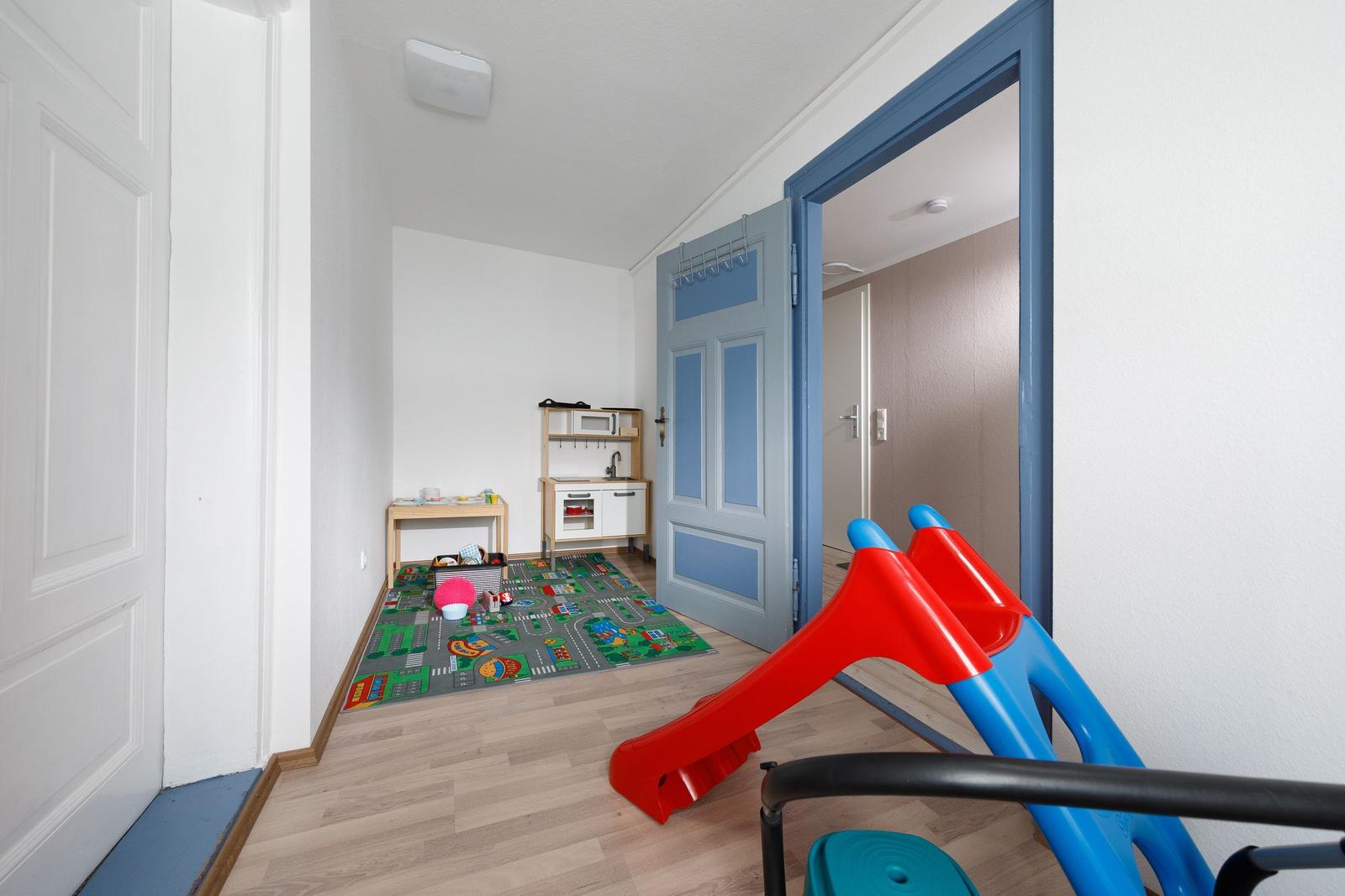 Kinderzimmer mit Spielteppich, Spielküche und Rutschbahn.