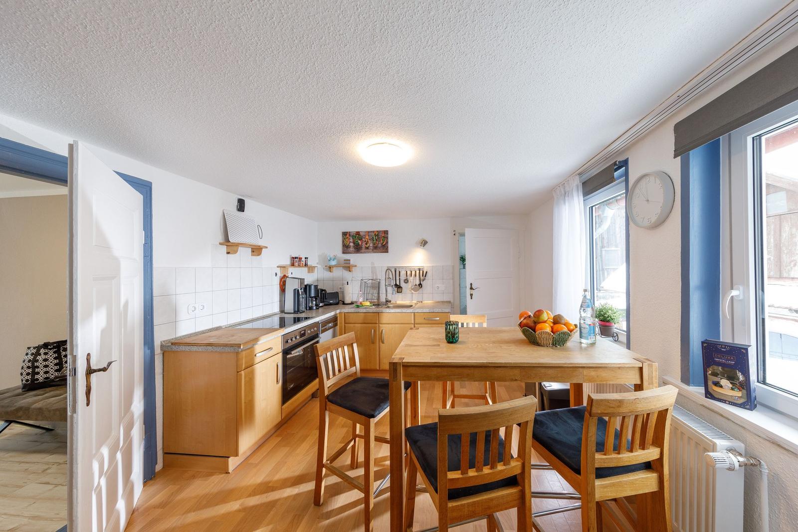 Küche mit Esstisch, Holzmöbel und Fenster. Tisch mit Obst und Wasser.