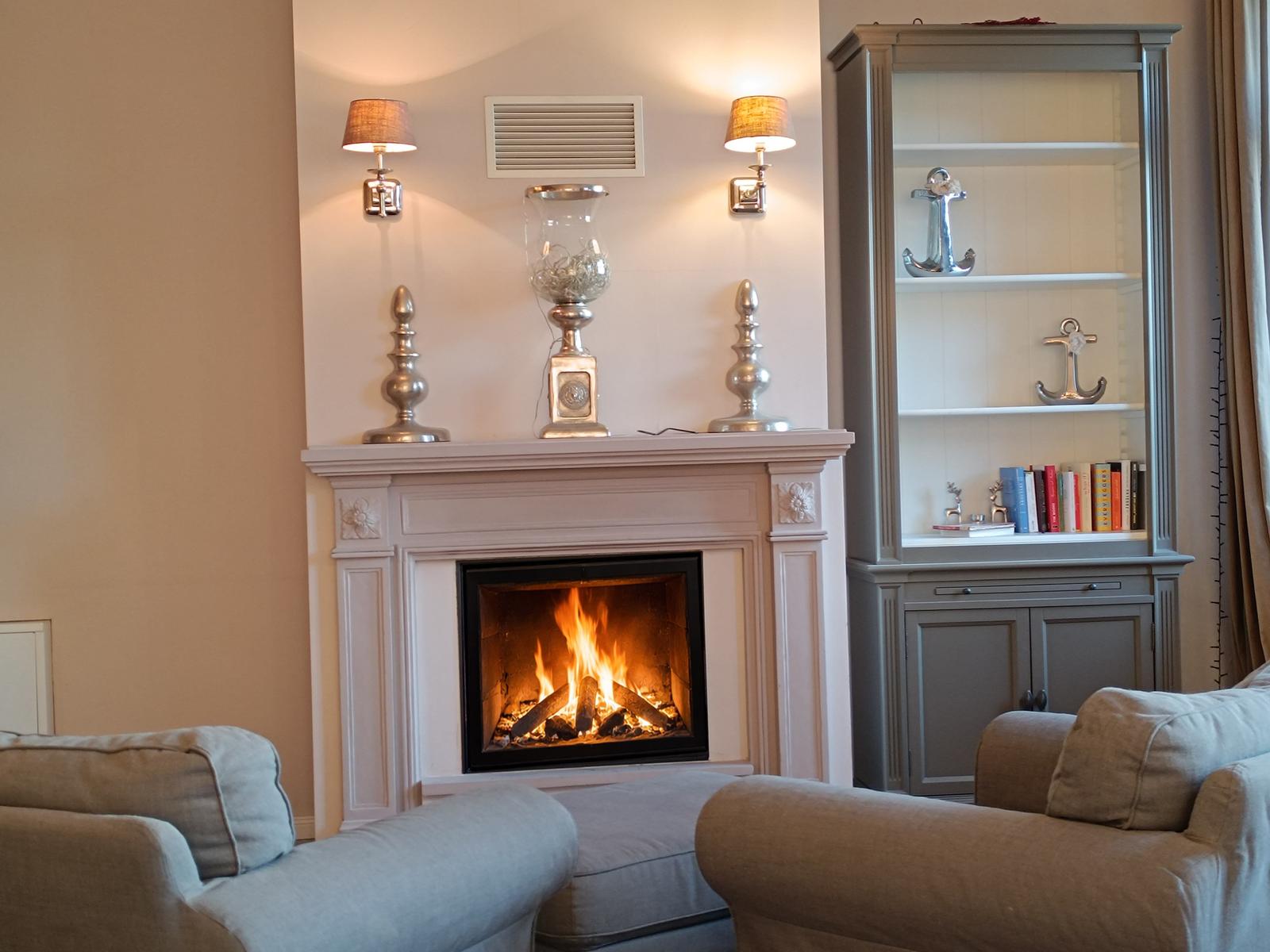 Ein Kamin mit brennendem Feuer, zwei Sessel und ein Schrank mit Ankerdekoration.