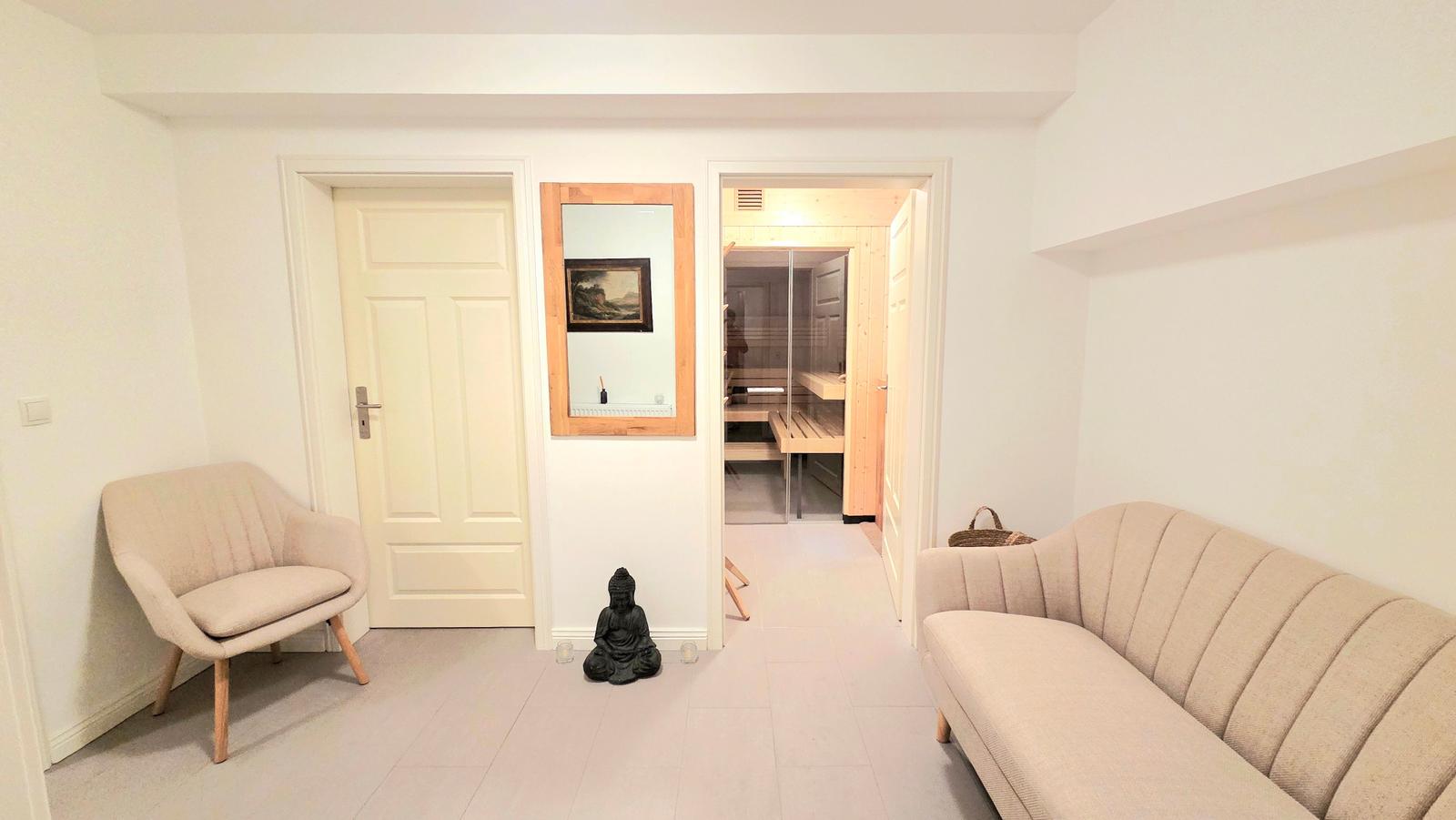 Wohnbereich mit Sofa, Sessel und Blick in die Sauna.