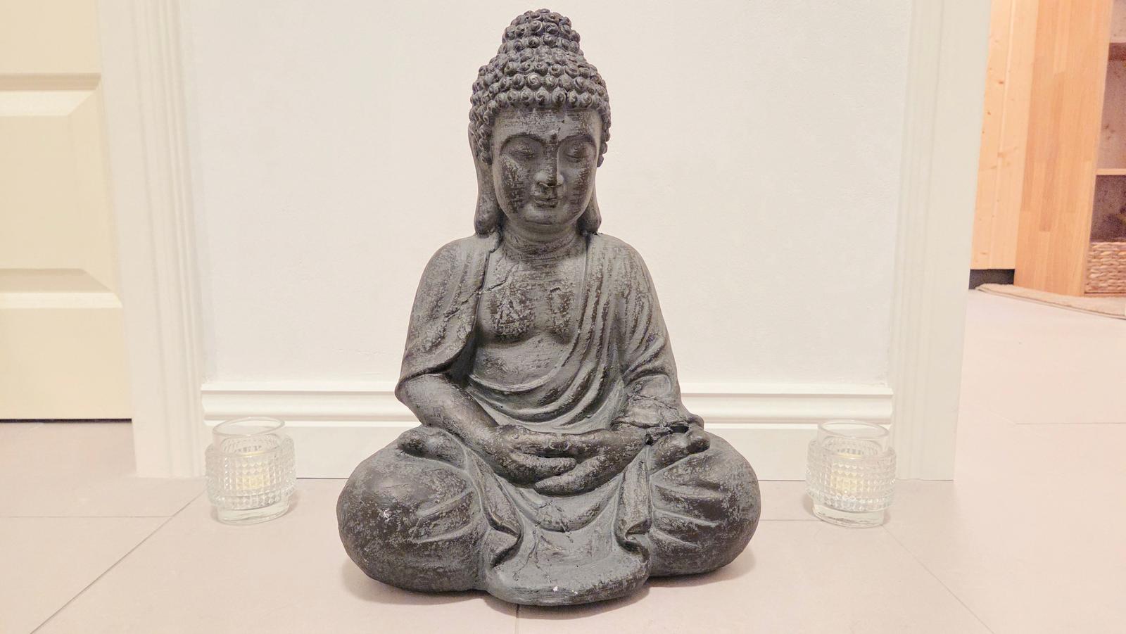 Eine Buddha-Statue sitzt auf dem Boden, flankiert von zwei Gläsern mit Kerzen.