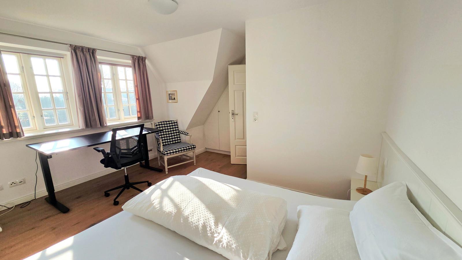 Schlafzimmer mit Bett, Schreibtisch und Fenster