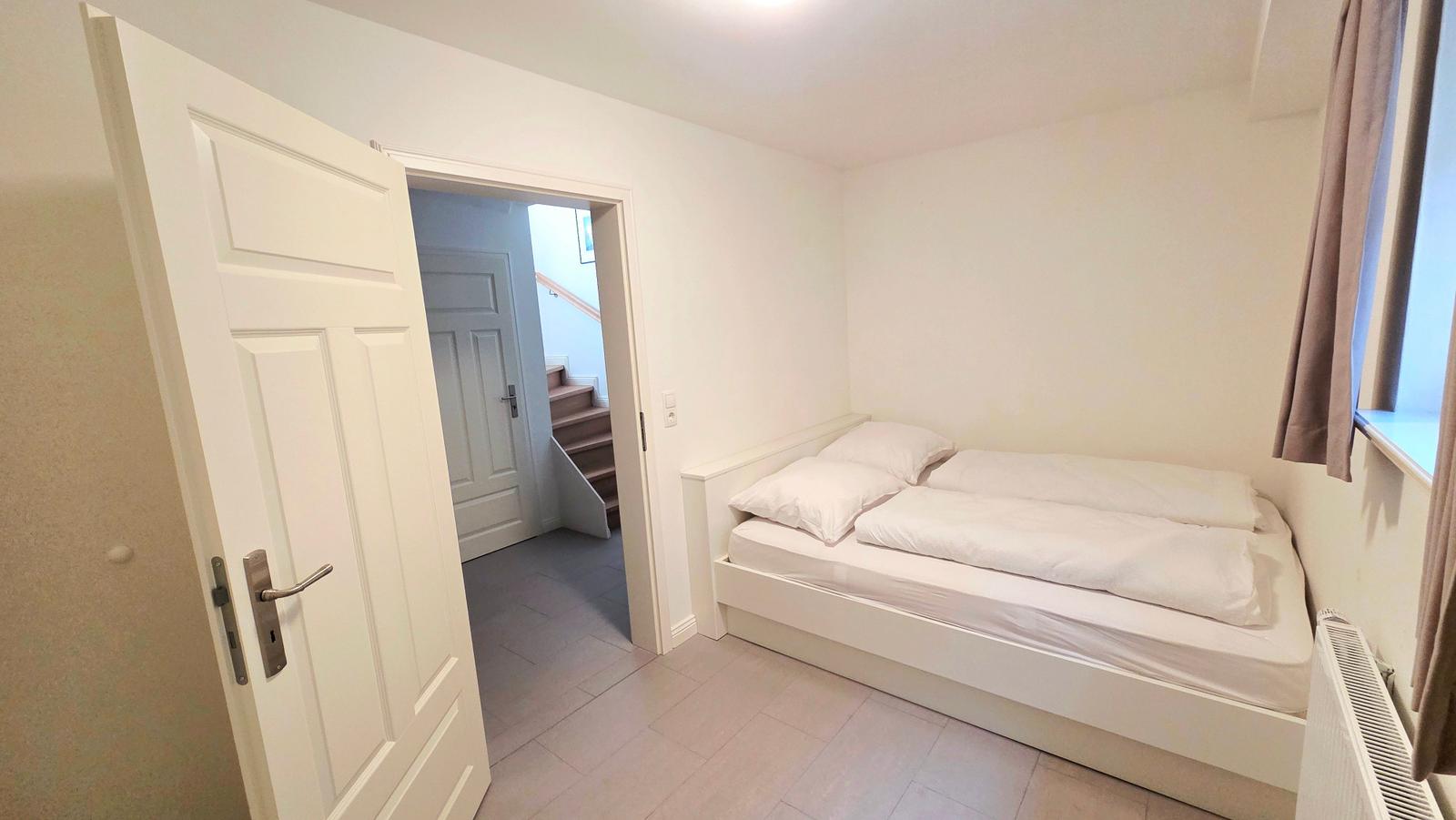 Schlafzimmer mit Doppelbett, Fenster und Tür zum Flur.