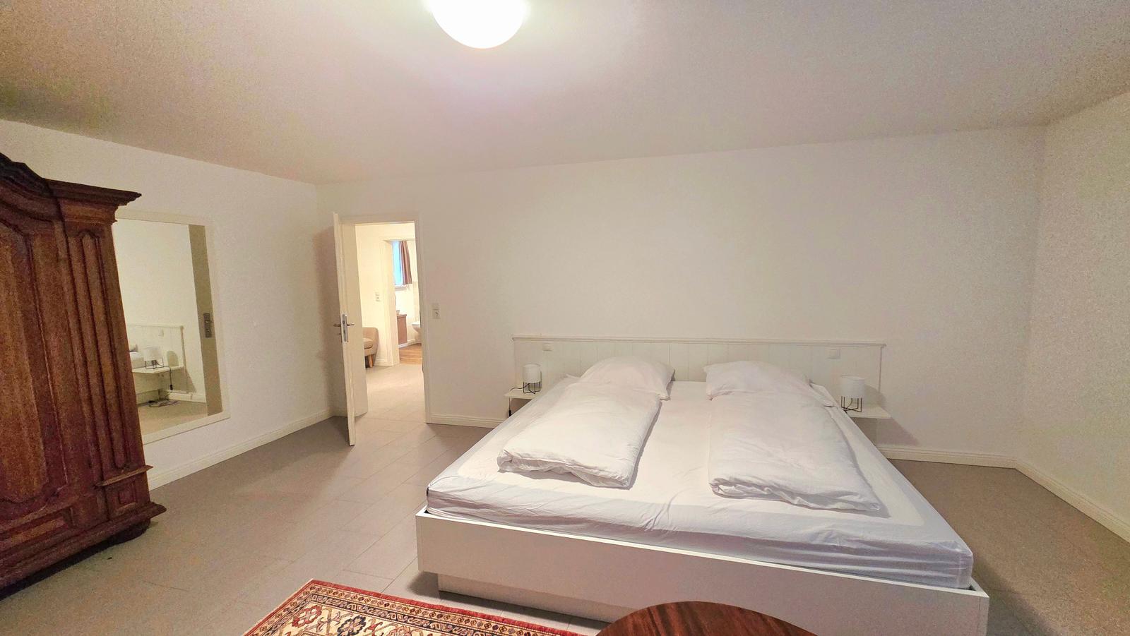 Schlafzimmer mit Doppelbett, Holzschrank und Blick in angrenzende Räume.