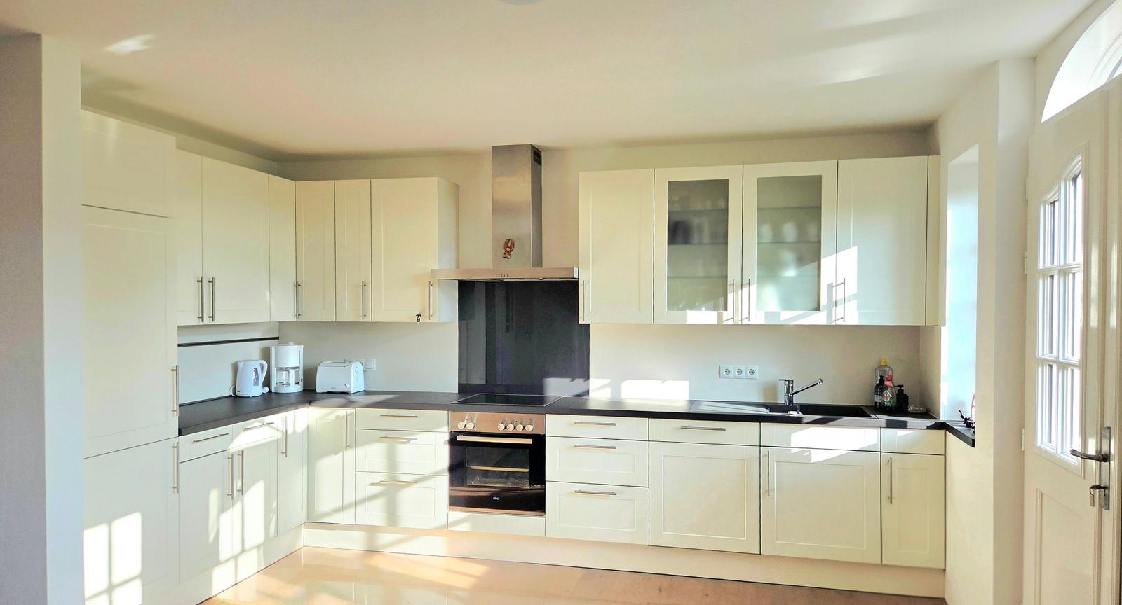 Küche mit weißen Schränken, dunklem Arbeitsplatz und integriertem Ofen.