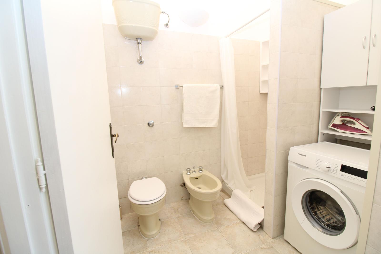 Bathroom with toilet, bidet, shower, and washing machine.