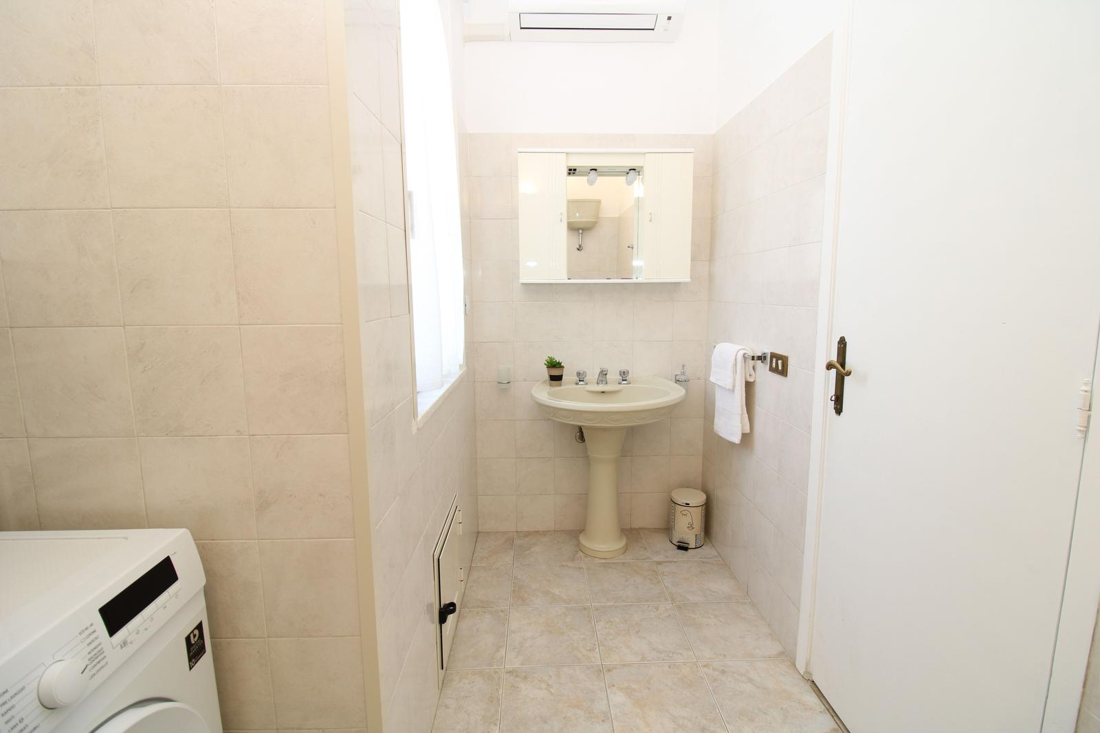 Bathroom with pedestal sink, mirror cabinet, and washing machine.