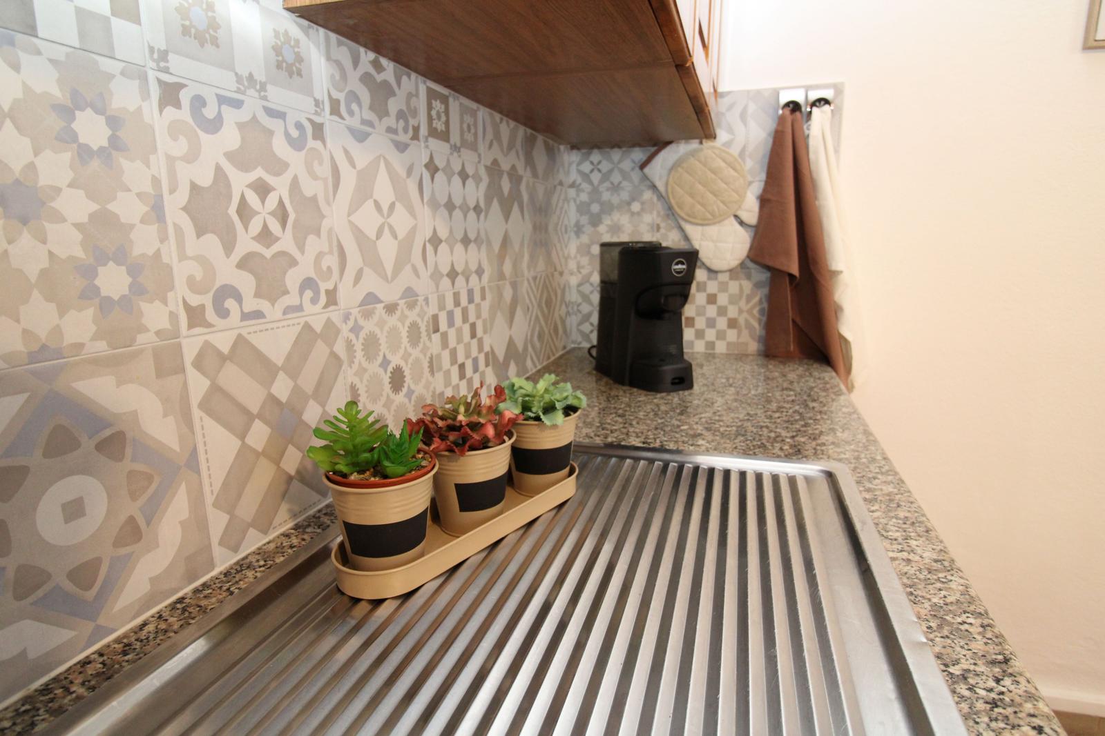 Kitchen counter with mosaic tiles, coffee machine, and potted plants.